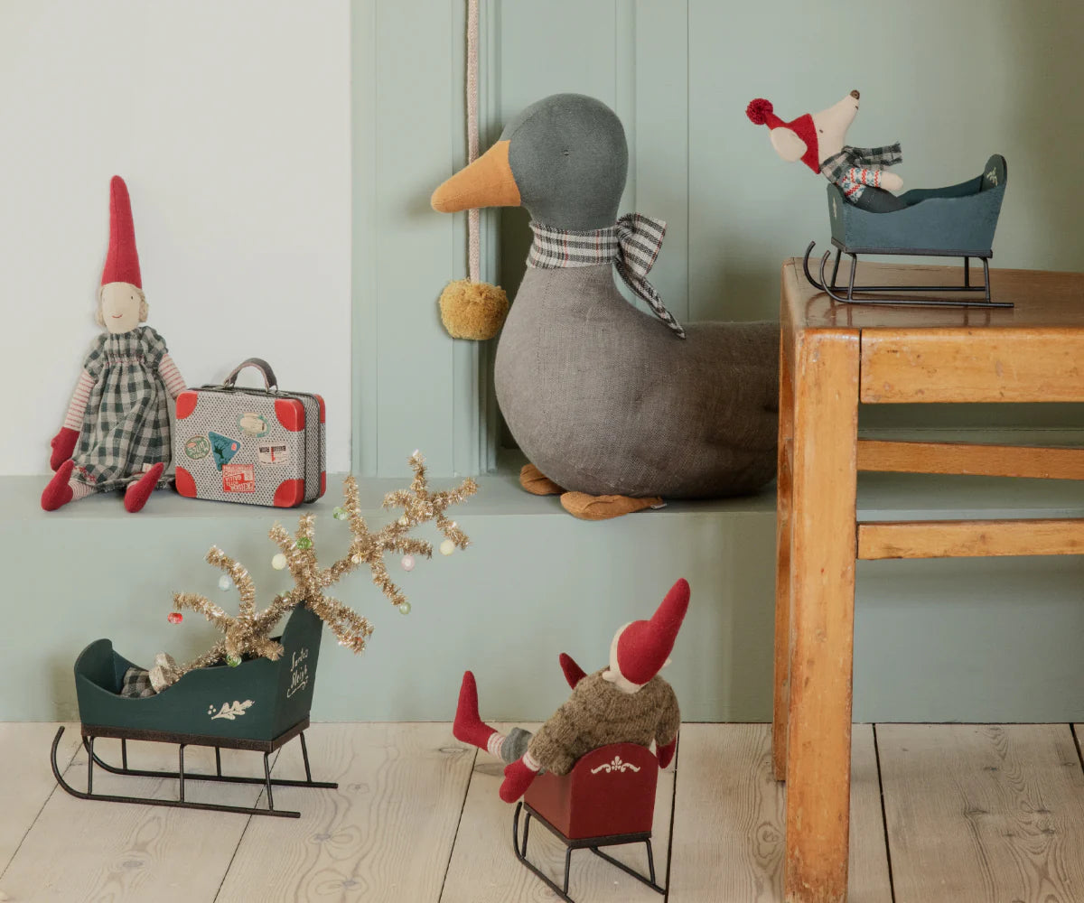 Decorative items including a duck, small figures, and sleds on a wooden floor against a light green wall. | Maileg uk