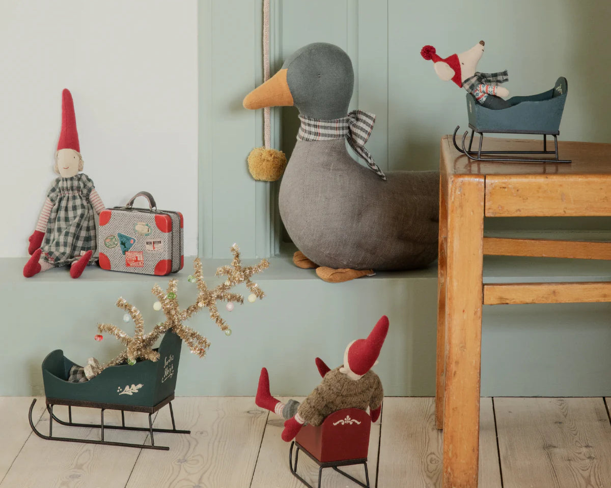 Decorative items including a duck, small figures, and sleds on a wooden floor against a light green wall. | Maileg uk