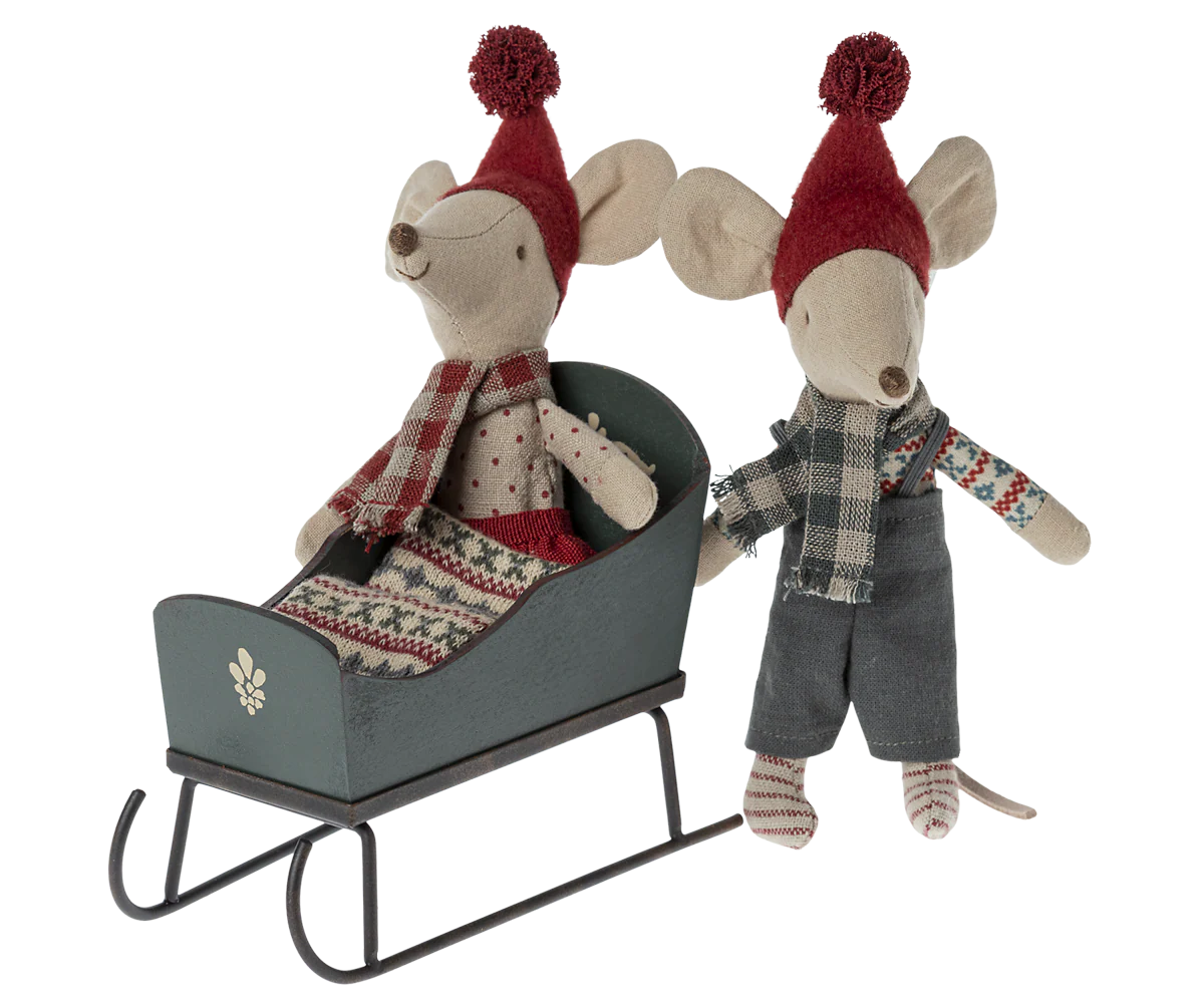 Two toy mice in festive attire with a miniature sleigh on a white background
