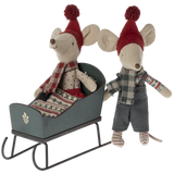 Two toy mice in festive attire with a miniature sleigh on a white background