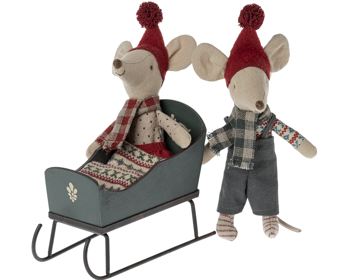 Two toy mice in festive attire with a miniature sleigh on a white background