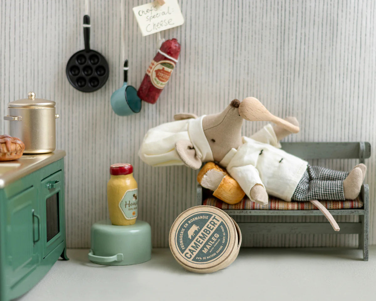 Toy chef mouse lying on a small bed in a miniature kitchen setting with various kitchen items around. |Chef clothes, Big sister and big brother mouse | Maileg UK