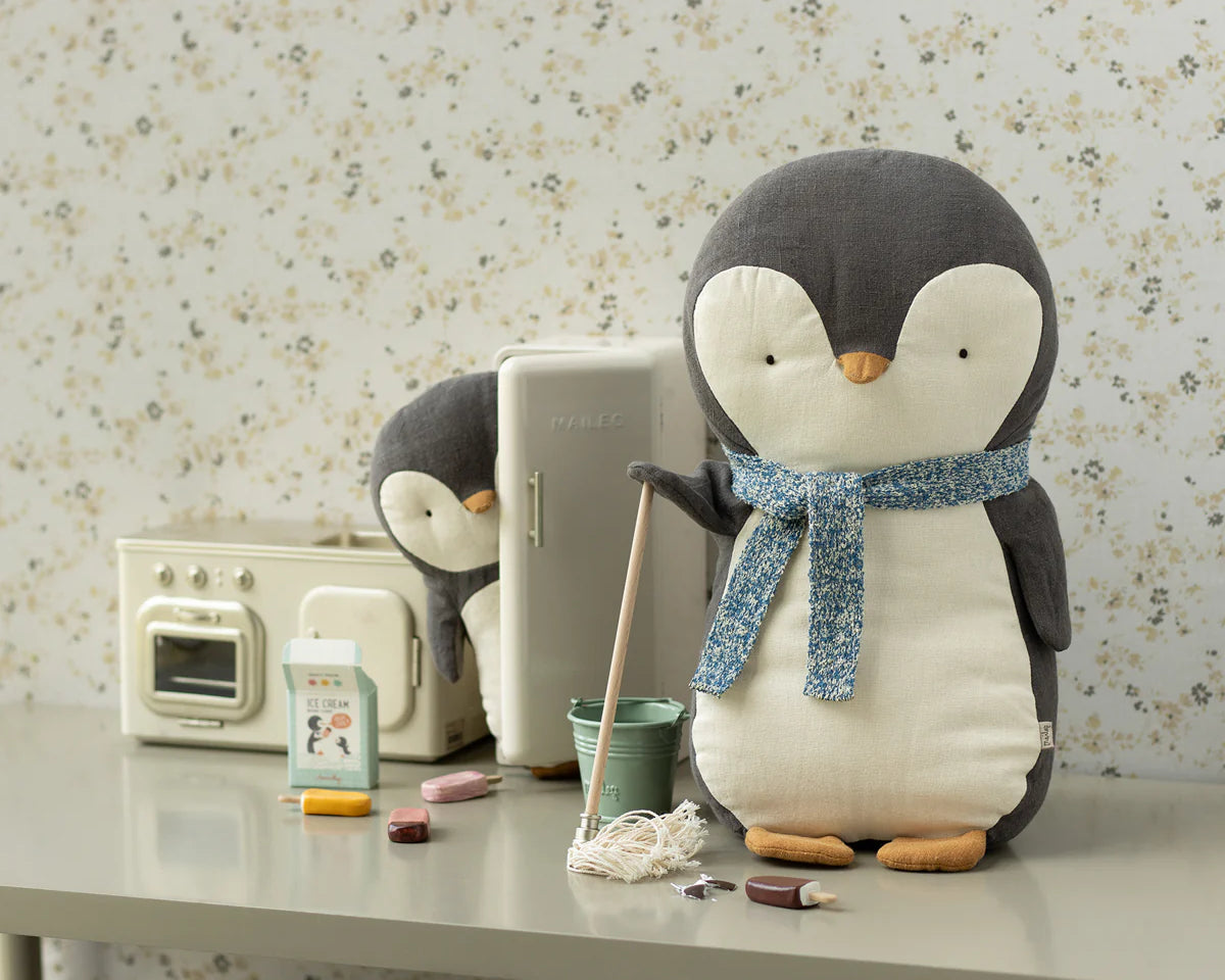 Plush penguin with a scarf on a table with a vintage radio and other items. | Maileg UK