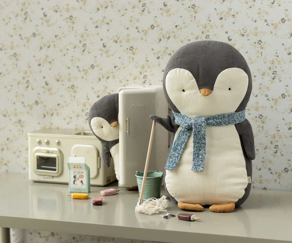Plush penguin with a scarf on a table with a vintage radio and other items. | Maileg UK