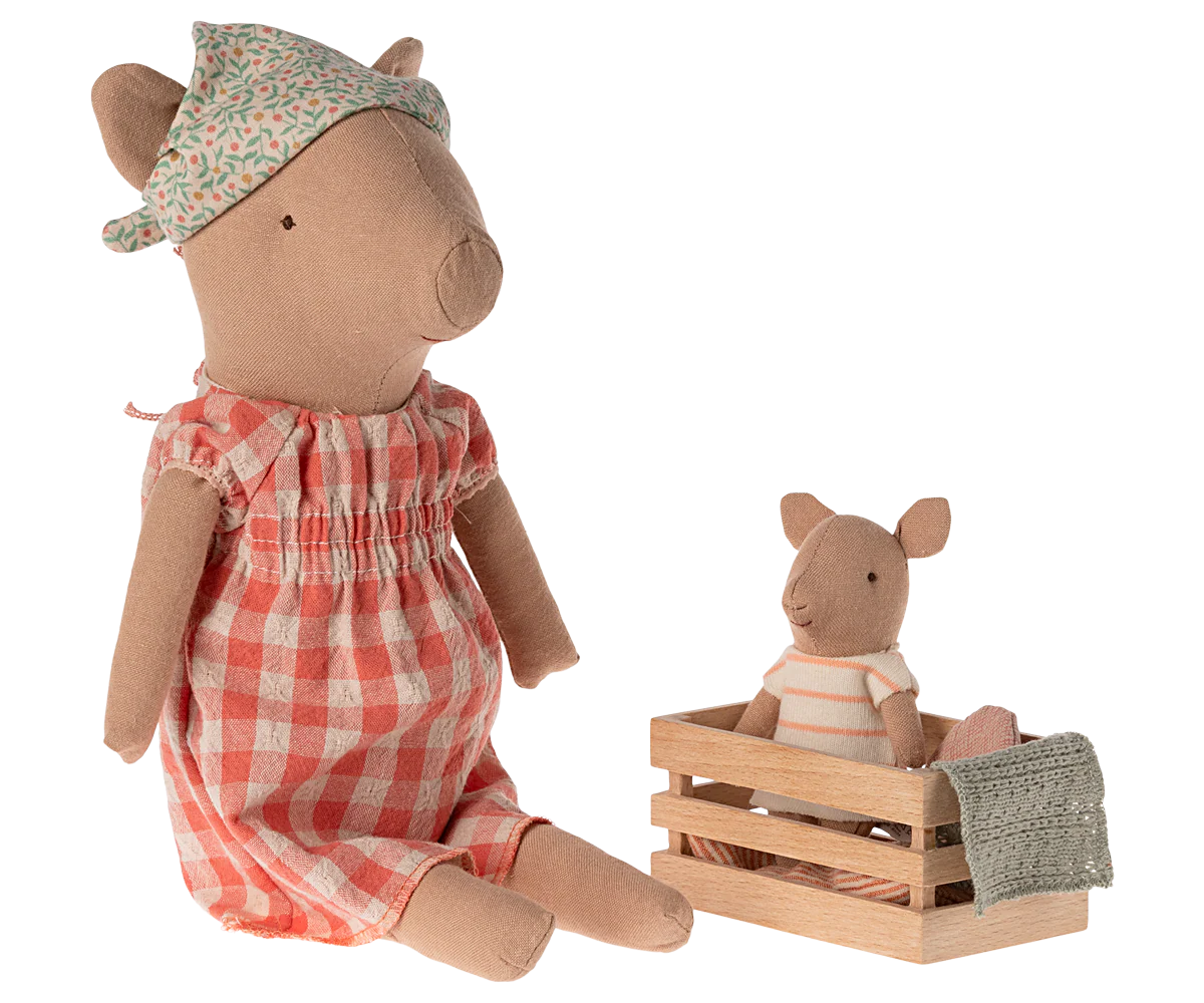 Two plush pig toys, one in a red checkered dress and floral hat, the other in a striped outfit sitting in a wooden crate. | Maileg UK