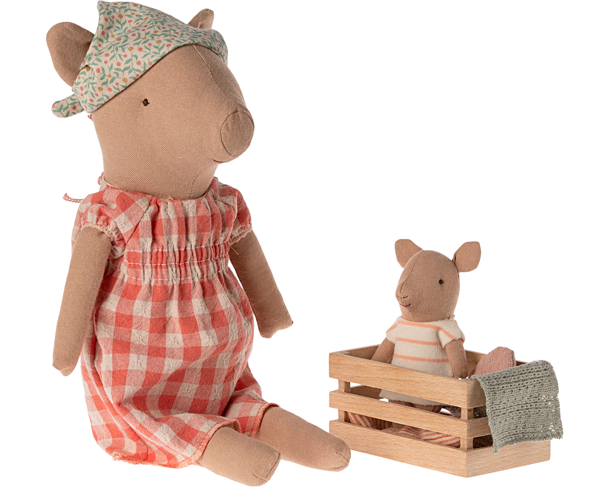 Two plush pig toys, one in a red checkered dress and floral hat, the other in a striped outfit sitting in a wooden crate. | Maileg UK