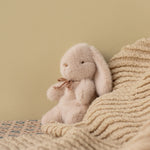 Plush bunny toy sitting on a textured blanket against a beige wall | Maileg UK