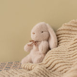 Plush bunny toy sitting on a textured blanket against a beige wall | Maileg UK