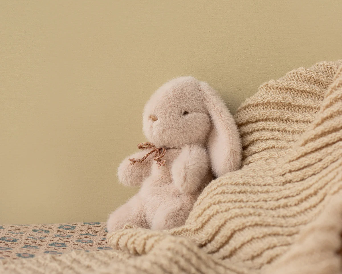Plush bunny toy sitting on a textured blanket against a beige wall | Maileg UK