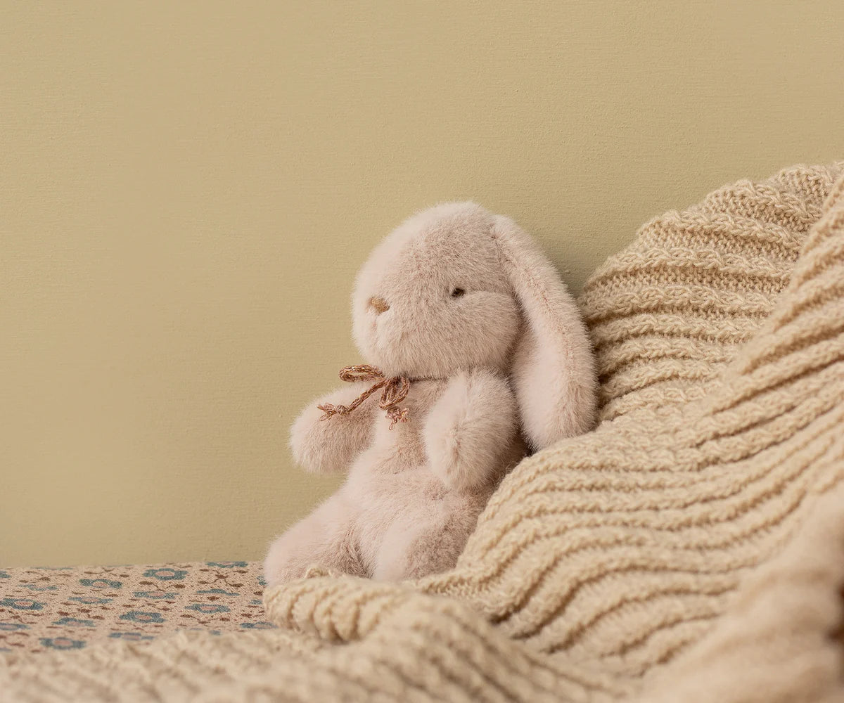 Plush bunny toy sitting on a textured blanket against a beige wall | Maileg UK