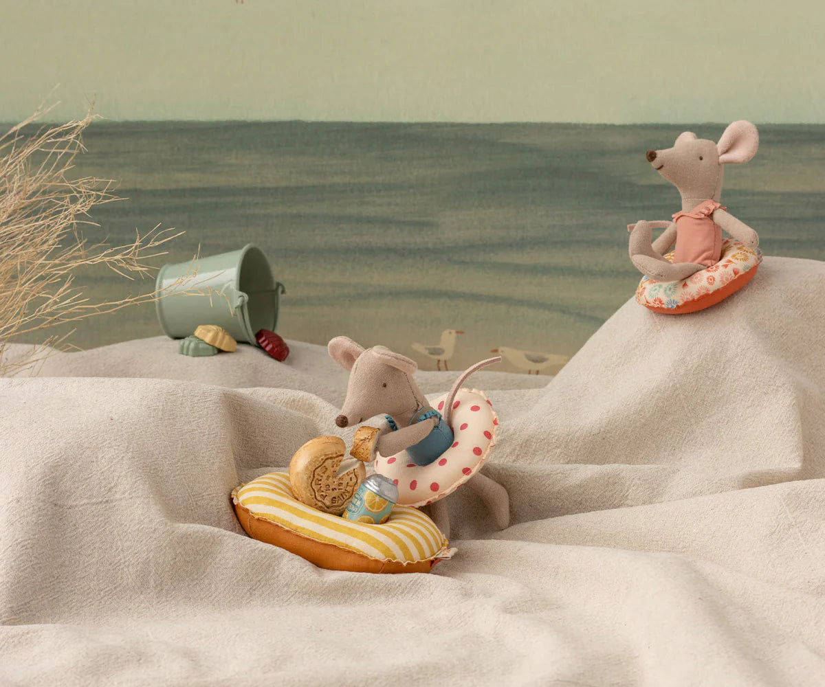 Two toy mice with beach accessories on a sandy surface with a scenic background. | Maileg UK