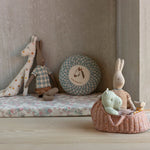 Children's toys including a giraffe, rabbit, and other plush items on a floral mattress against a neutral wall. | Maileg UK