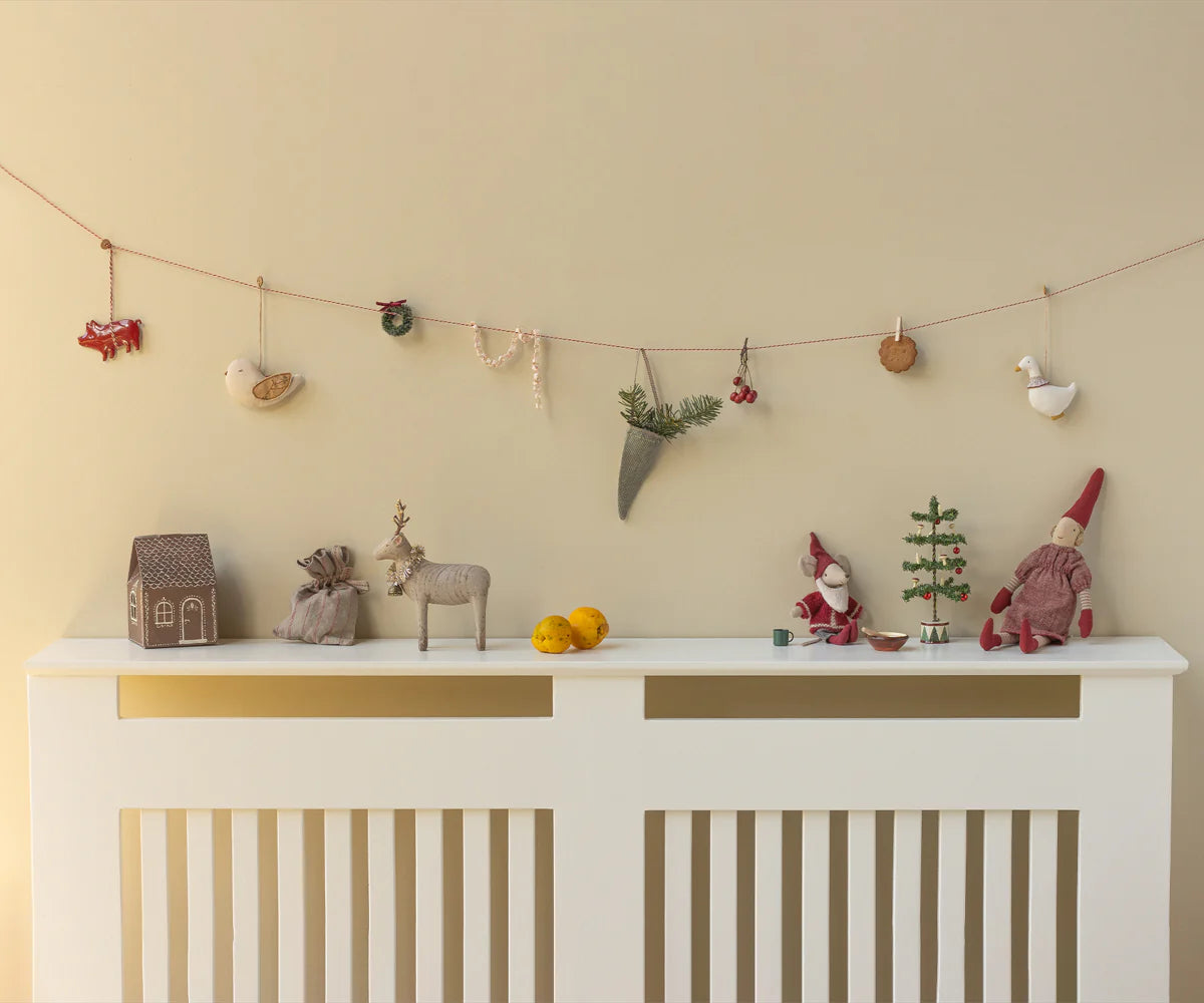 Decorative items on a white console table against a beige wall with a string of small ornaments. | Christmas Maileg UK