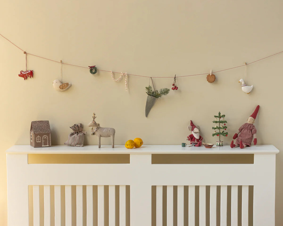 Decorative items on a white console table against a beige wall with a string of small ornaments. | Christmas Maileg UK