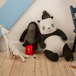 Plush toys including a panda, elephant, and giraffe on a wooden floor with a chair and toy box in the background. | Maileg UK
