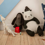 Plush toys including a panda, elephant, and giraffe on a wooden floor with a chair and toy box in the background. | Maileg UK