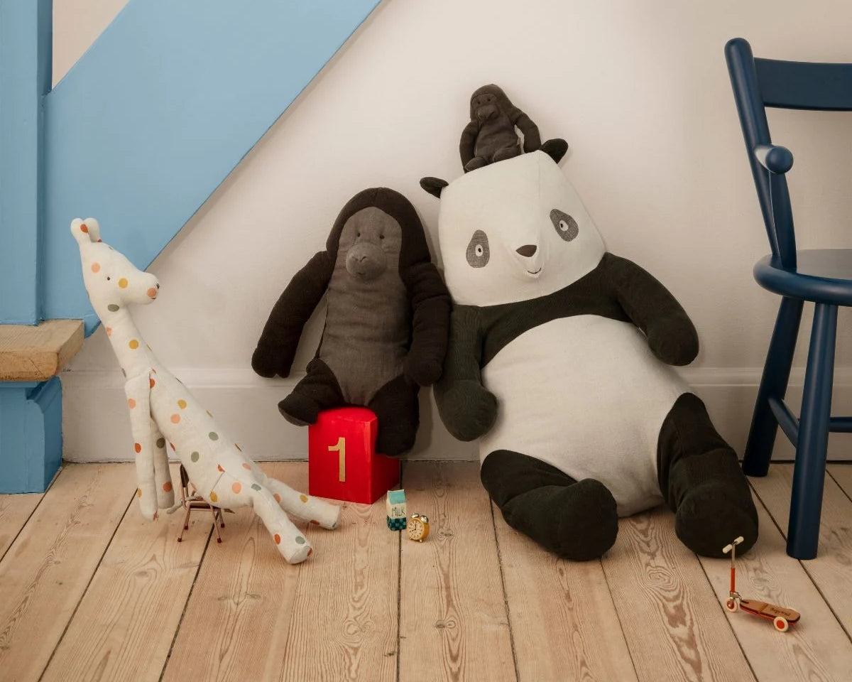 Plush toys including a panda, elephant, and giraffe on a wooden floor with a chair and toy box in the background. | Maileg UK