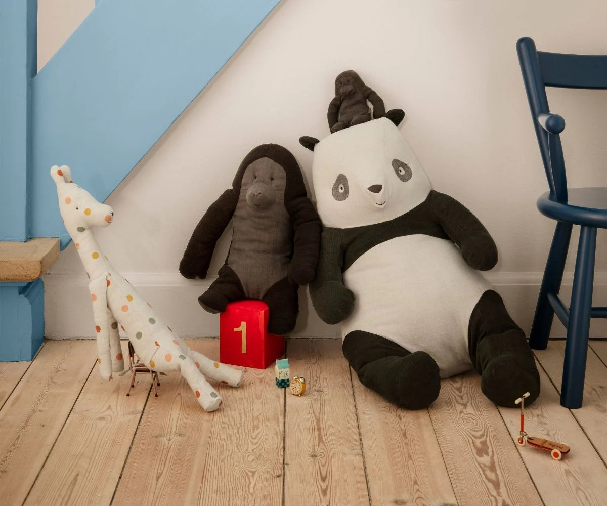 Plush toys including a panda, elephant, and giraffe on a wooden floor with a chair and toy box in the background. | Maileg UK
