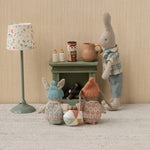 Toy figures of a rabbit, bear, and gnome around a small table with a lamp and jars on a textured surface.