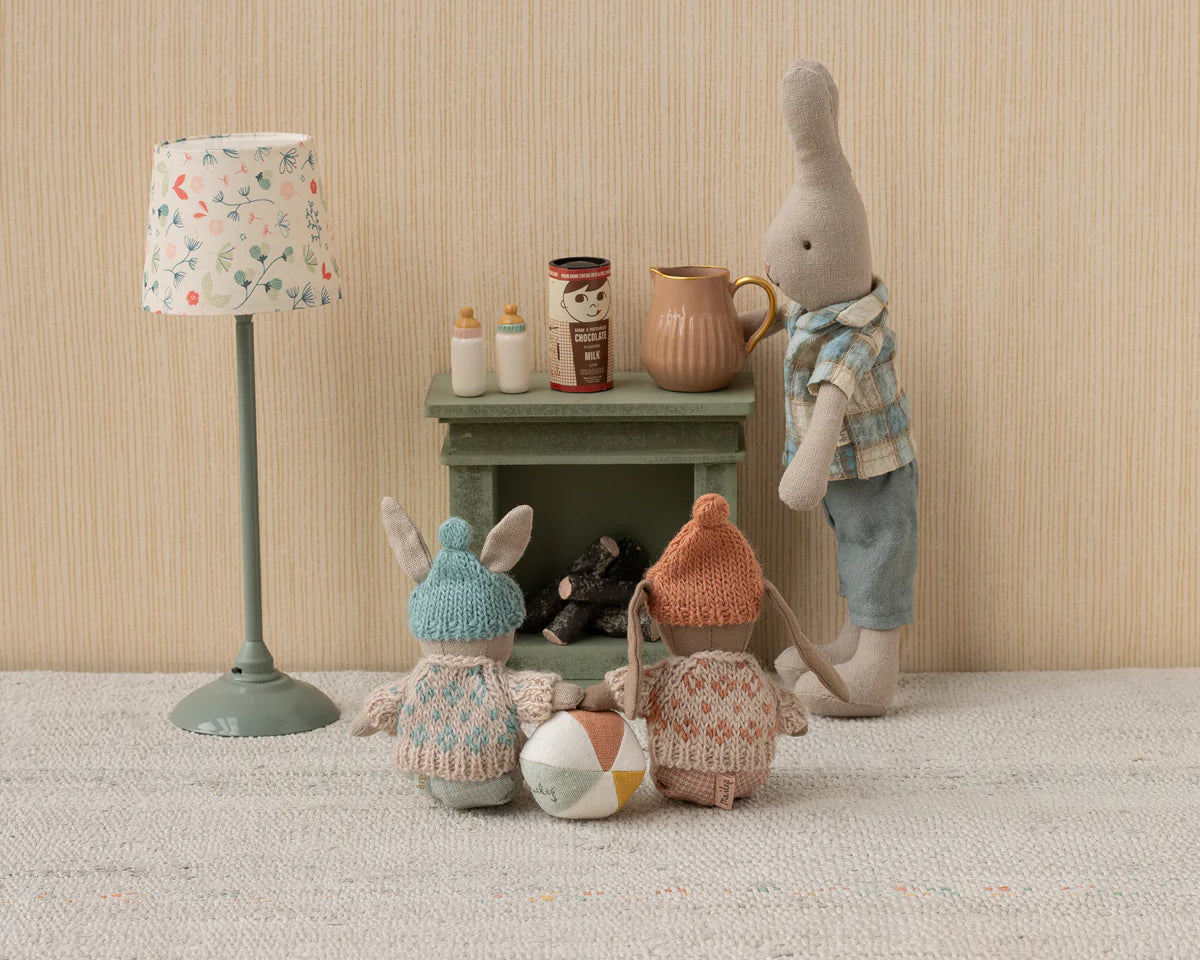 Toy figures of a rabbit, bear, and gnome around a small table with a lamp and jars on a textured surface.