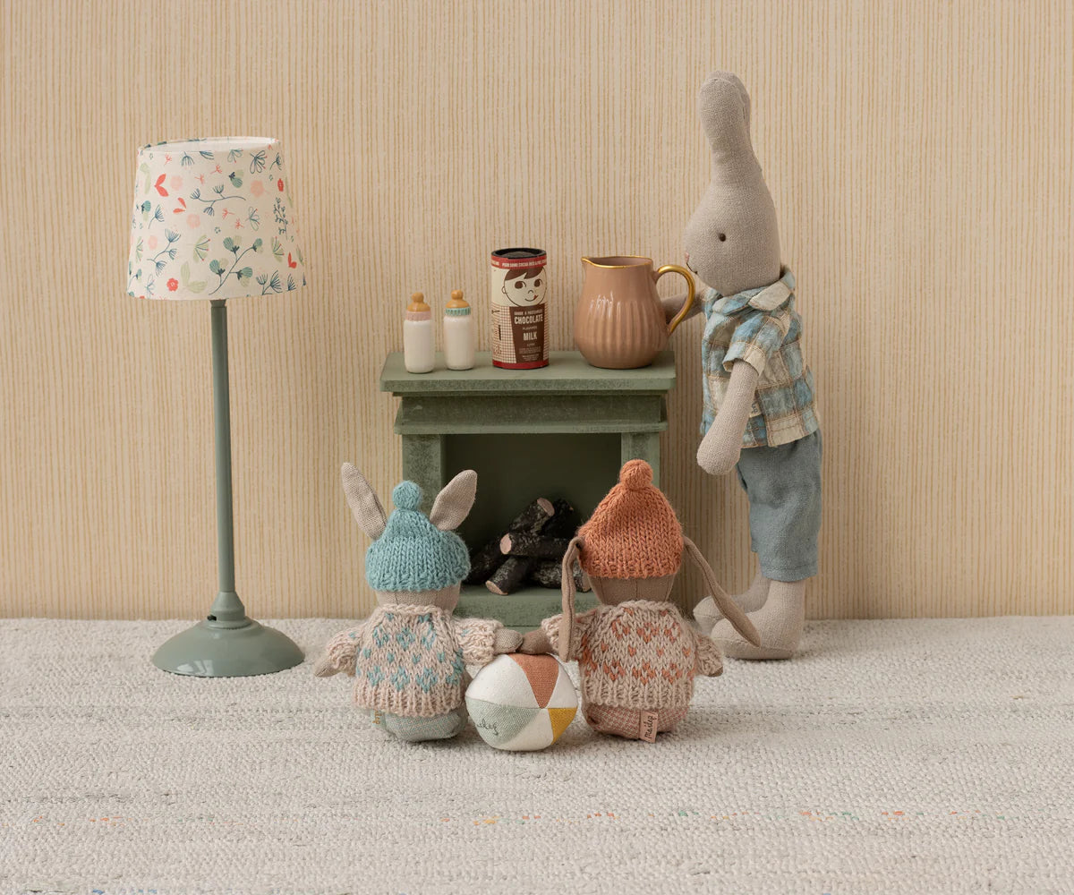 Toy figures of a rabbit, bear, and gnome around a small table with a lamp and jars on a textured surface.