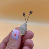 Small wooden bid vase held between fingers against a blurred background