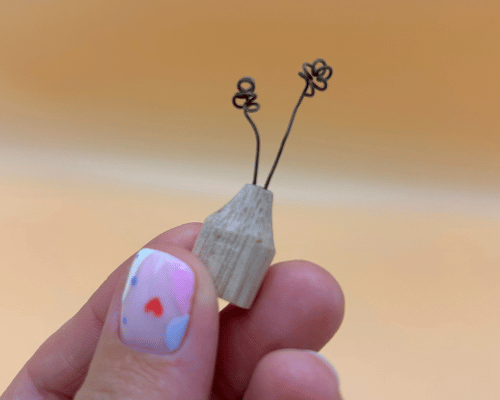Small wooden bid vase held between fingers against a blurred background
