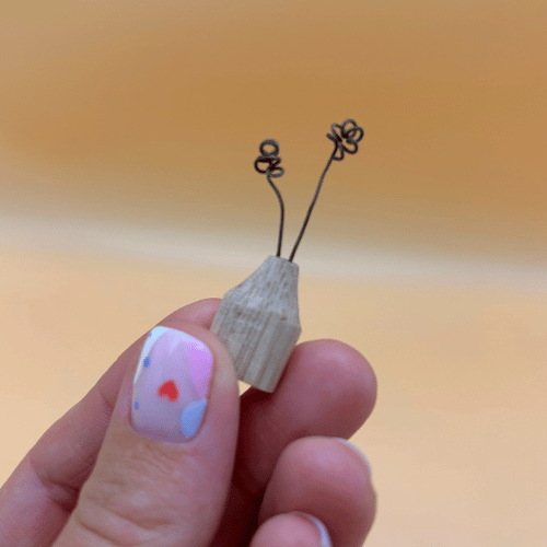 Small wooden bid vase held between fingers against a blurred background
