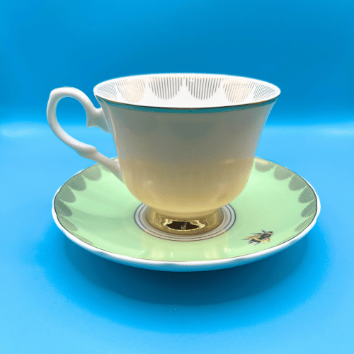 Yvonne Ellen Boozy cup and saucer viewed from the back peach tea cup with gold accents and pastel green saucer decorated with a bumble bee. Quintessential british tea party material.