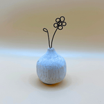 Small textured ceramic vase with a wire flower on a light background