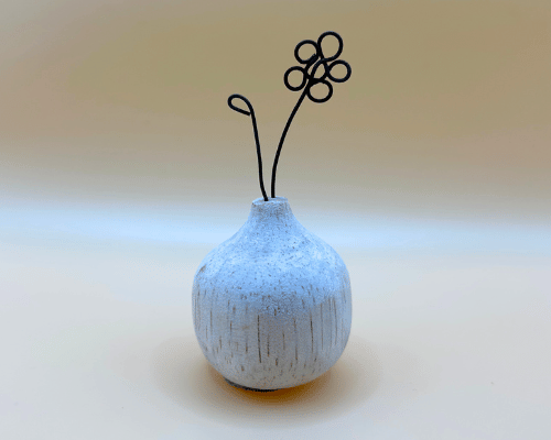 Small textured ceramic vase with a wire flower on a light background