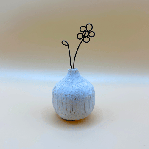 Small textured ceramic vase with a wire flower on a light background