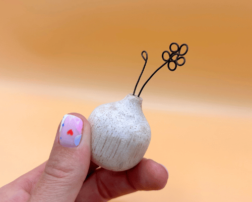 Small white ceramic vase with black decorative elements held by a hand against an orange background
