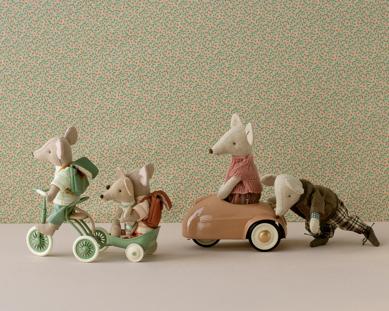 The Maileg mice are going on an adventure, 3 mice on the green tricycle and trailer while mummy mouse sits in the coral car that daddy mouse is pushing.