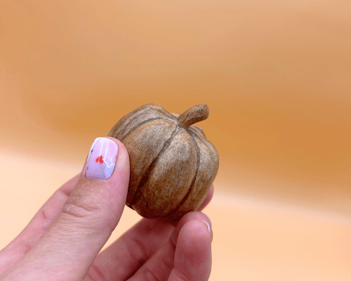 Hand holding a small brown gourd against a blurred orange background