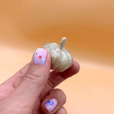 Hand holding a small decorative pumpkin against a warm orange background