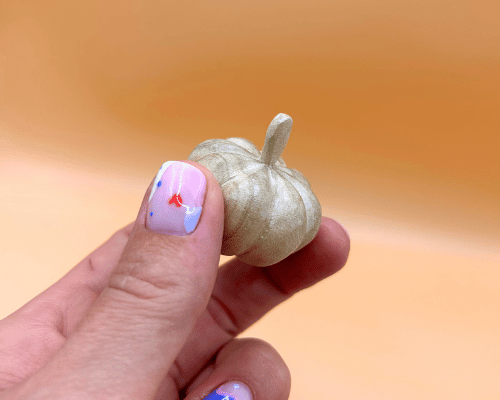Hand holding a small decorative pumpkin against a warm orange background