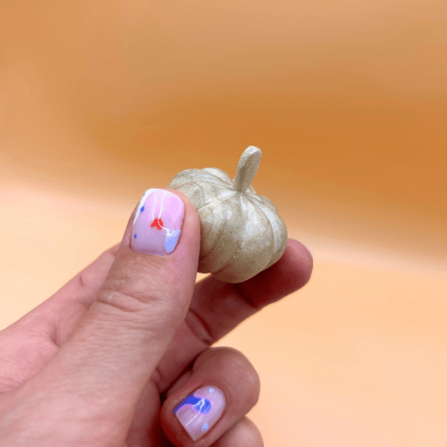 Hand holding a small decorative pumpkin against a warm orange background