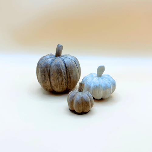 Three decorative pumpkins on a white surface with a blurred background